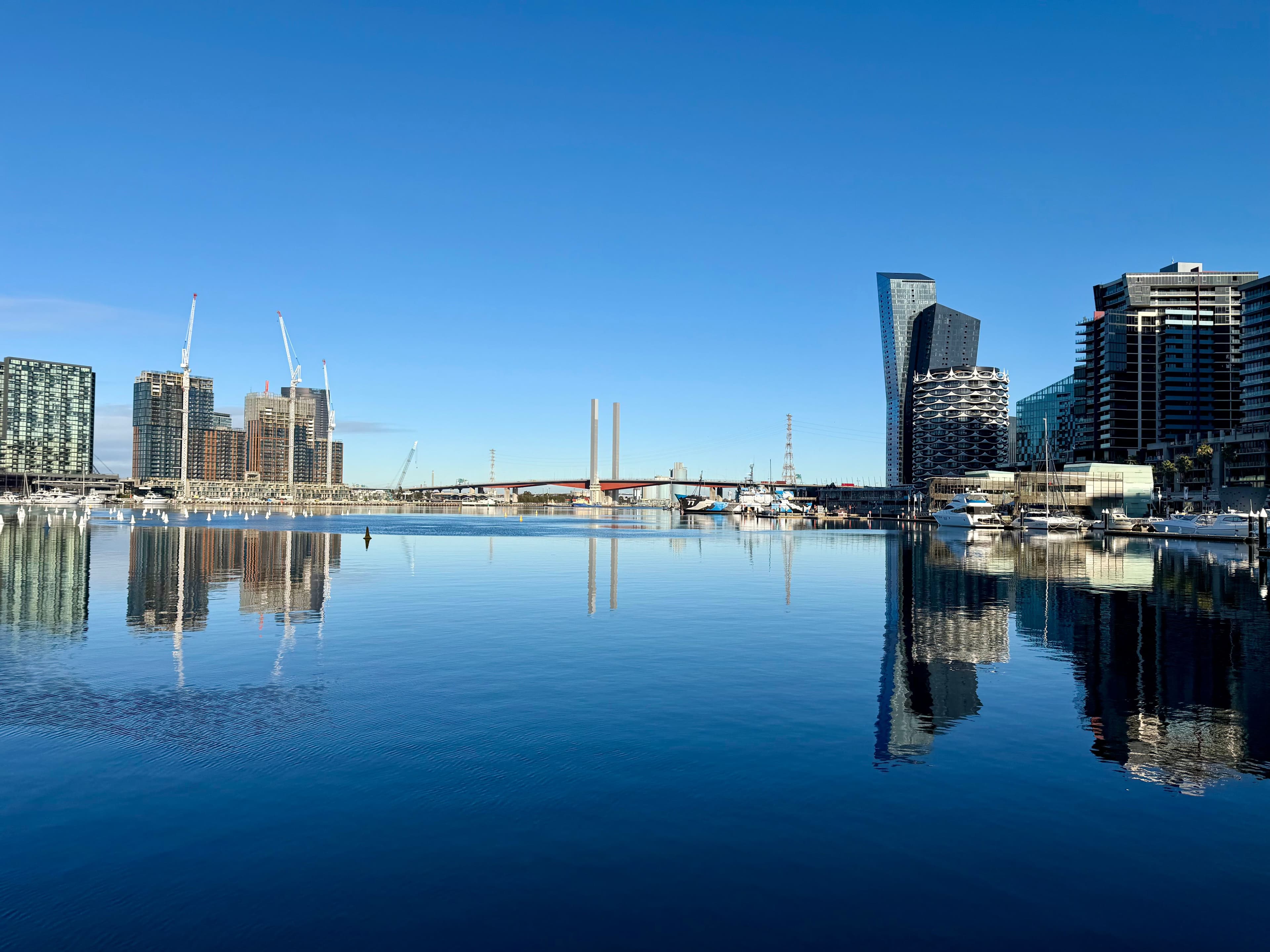 A waterfront city skyline and marina mirrored in calm harbour water